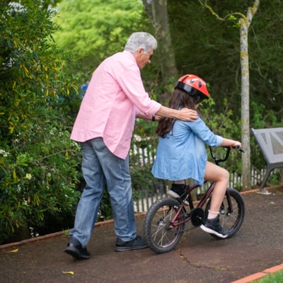 Individual walking along with their grandchild on a bicycle. 