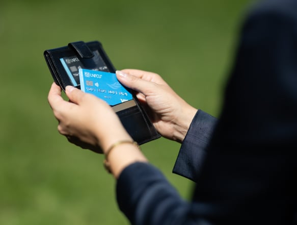 Individual holding a wallet with UNFCU Elite and Azure credit cards.